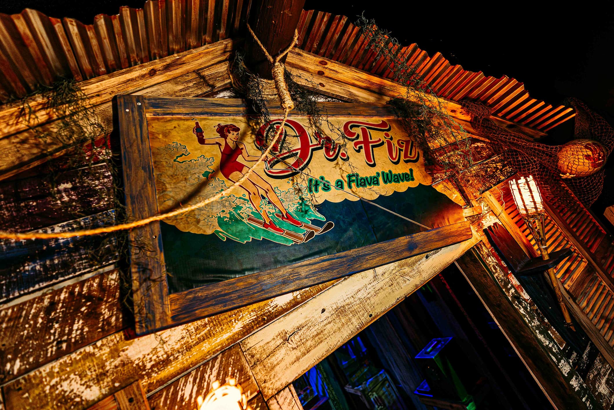 A weathered sign over a tiki bar entrance reads "Dr. Fiz" in a retro script with a picture of a woman water skiing.
