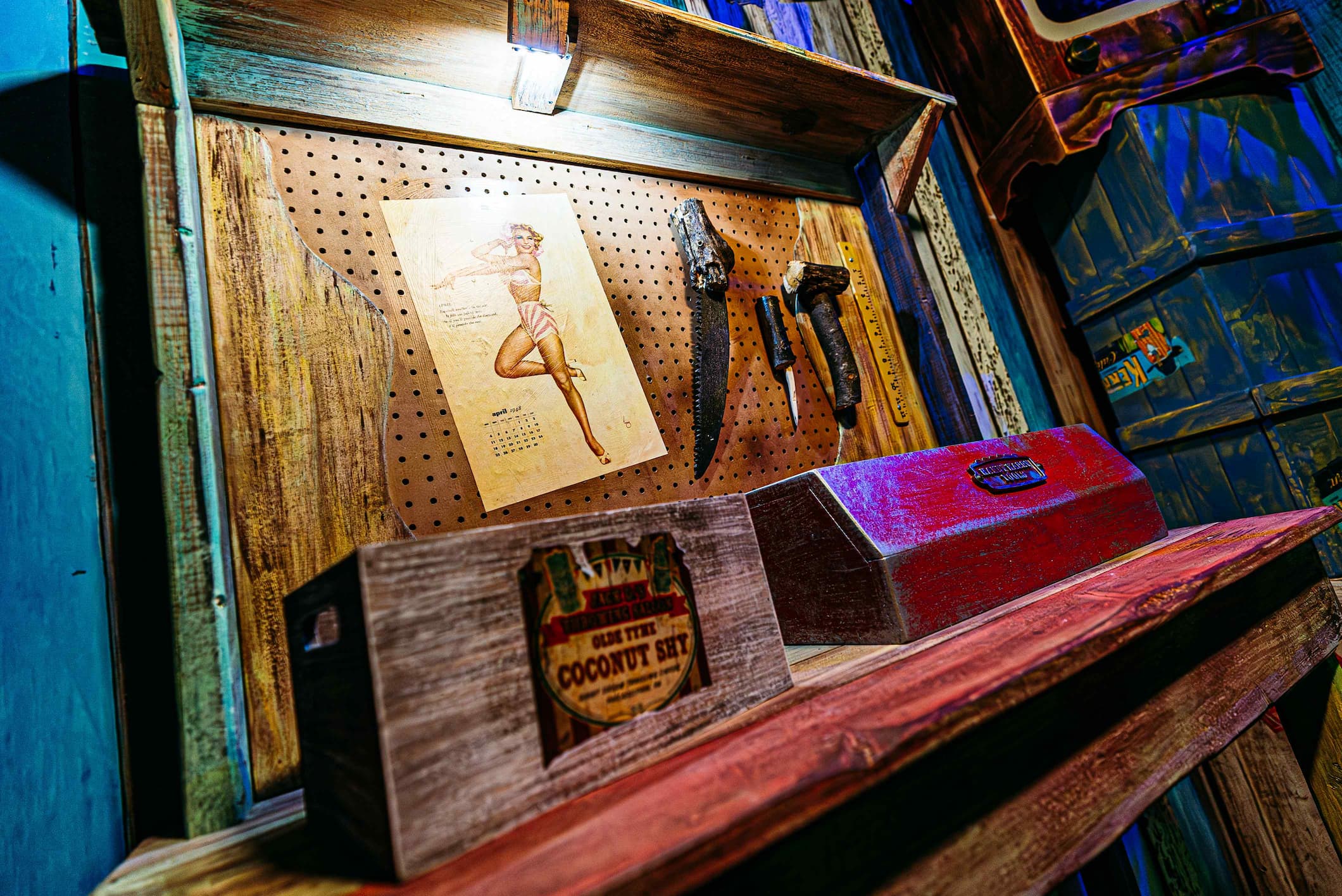 A wooden shelf holds a pin-up girl calendar, tools, and a box labeled "Coconut Shy".
